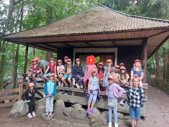 Das Bild zeigt eine Gruppe von Kindern, die für ein Gruppenbild vor einem Haus im Wald posieren.  