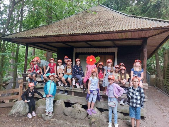 Das Bild zeigt eine Gruppe von Kindern, die für ein Gruppenbild vor einem Haus im Wald posieren.