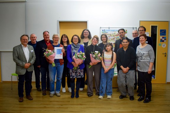 Das Foto zeigt ein Gruppenbild mit 14 Personen, 3 von ihnen halten einen Blumenstrauß vor sich.  