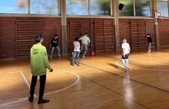 Das Bild zeigt mehrere Kinder, die in einer Turnhalle etwas spielen.