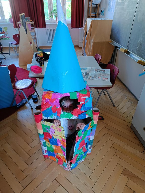 Das Bild zeigt eine Rakete aus Pappkartons, daraus schaut ein Kind heraus.