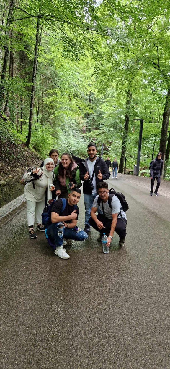 Man sieht eine Gruppe von Menschen auf einer Straße durch den Wald posieren und in die Kamera grinsen. 
