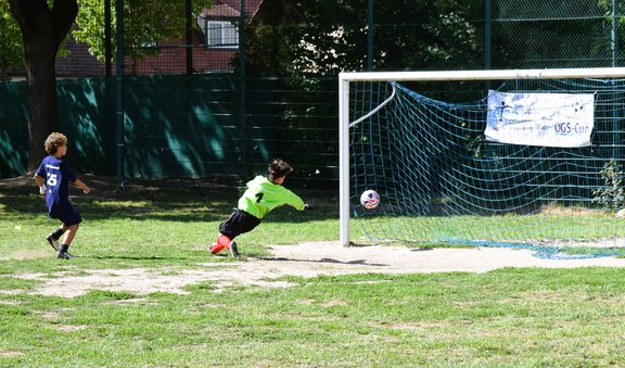 Das Bild zeigt zwei fußballspielende Kinder, eines im Tor, das andere schießt auf das Tor.  
