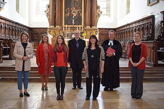 Das Bild zeigt sieben Männer und Frauen vor einem Altar in einer Kirche.