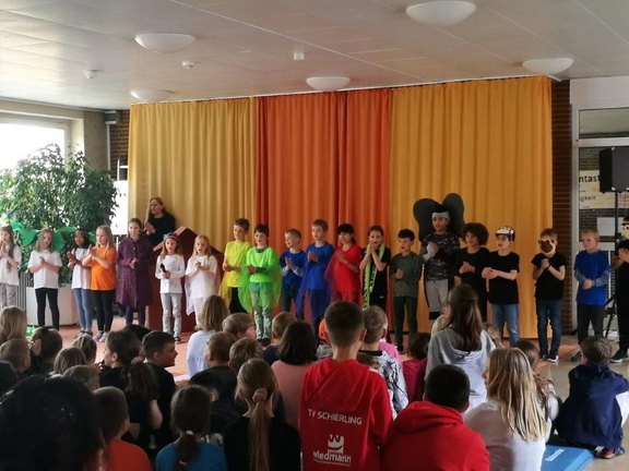 Das Bild zeigt mehrere Kinder, die ein Theaterstück aufführen. Alle stehen in einer Reihe und klatschen.