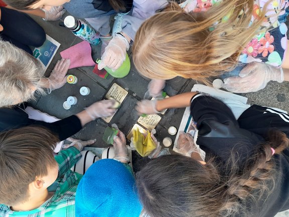 Das Bild zeigt eine Gruppe Kinder von oben, wie sie eifrig die Messingplatten am Boden.
