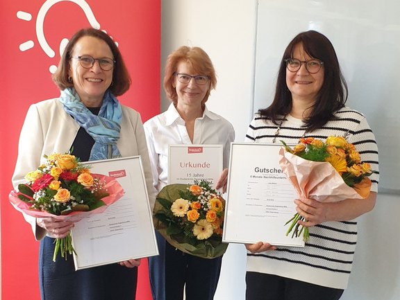Das Bild zeigt drei Frauen mit Blumensträußen bei der Übergabe der Stipendien