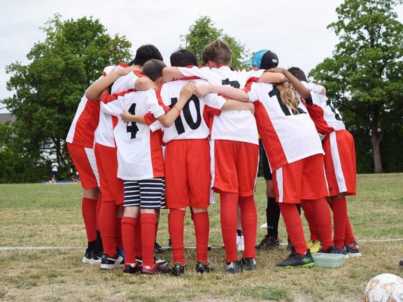 Es sind Kinder in mit Sporttrikots in einer Gruppenumarmung zu sehen.