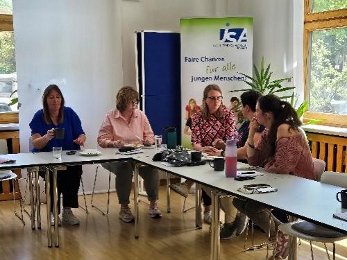 Das Bild zeigt eine Gruppe von fünf Menschen am Tisch sitzen.   