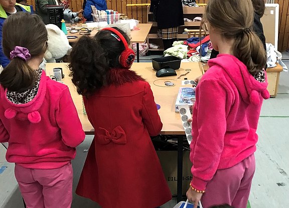 Das Bild zeigt drei Kinder von hinten an einem Tisch.  