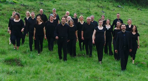 Das Bild zeigt eine Gruppe dunkel gekleideter Menschen auf einer grünen Wiese. 