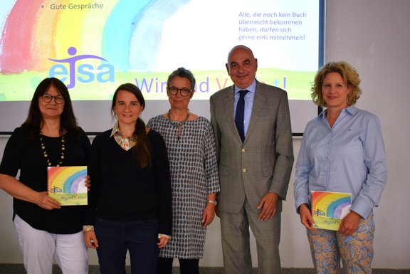 Das Bild zeigt 5 Personen, darunter 3 Frauen und 2 Männer, 2 von ihnen halten ein Buch in die Kamera.  