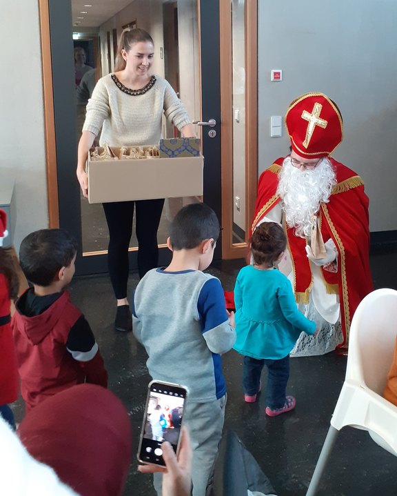 Der Nikolaus besucht die Kinder und eine Frau hält Geschenke bereit.  