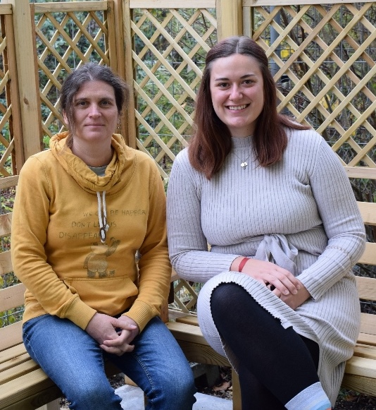 Das Bild zeigt zwei Frauen, die in einem Holzpavillon sitzen.