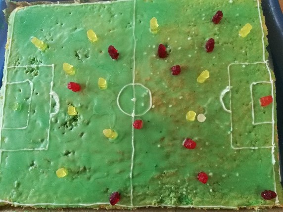 Das Bild zeigt einen Kuchen mit Gummibärchen, der einem Fußballfeld mit Spielern nachvollzogen ist.